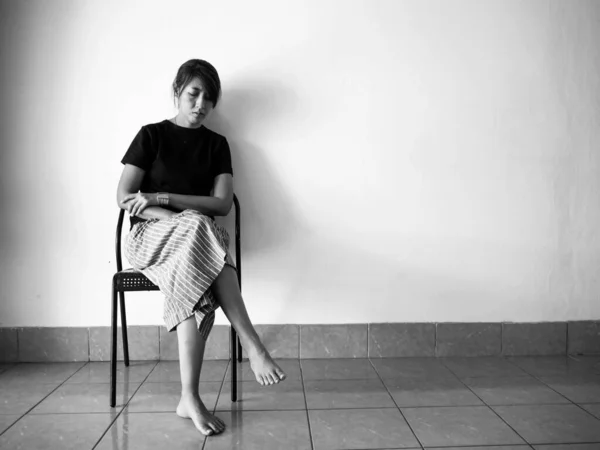 Stressed woman sitting on chair at the left side of wall,with upset and unhappy feeling,depressive disorder syndrome,serious emotion,black and white tone