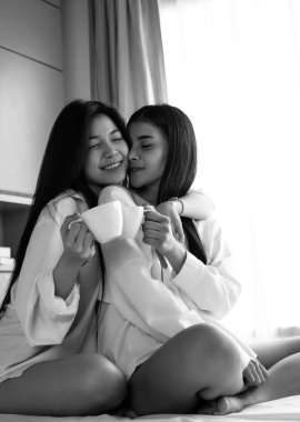 Yatakta oturan iki güzel bayan. Birlikte kahve içiyorlar, mutlu hissediyorlar. Romantik bir aşk çifti.