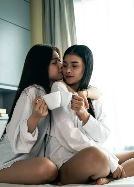 Two beautiful ladies sitting on bed.drinking coffee together,with happy feeling.Romantic love couple,good friendship