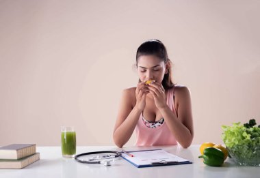 Portakal yiyen genç ve güzel bir bayan. Stethoscope ve diyet planının yanına konmuş bir bardak meyve suyu. Sağlıklı bir kadın.