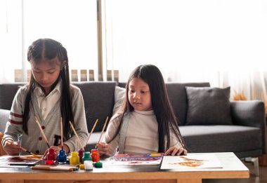 İki küçük kız renkli su rengini kağıda boyarlar.