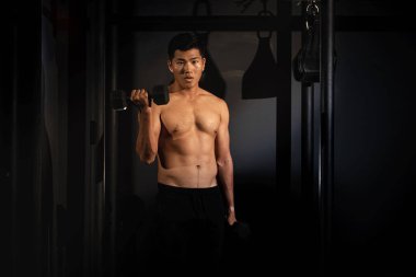 Yakışıklı adam, sağ eliyle dambıl kaldırıyor, kaslı, formda ve sıkı vücut için egzersiz yapıyor.