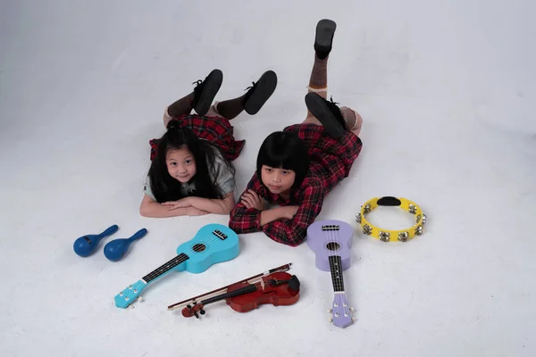stock image Two little girl laying down on ground floor.Beside ukulele,violin,Maracas and Tambourine,doing activity together