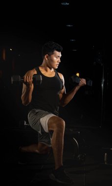 Yakışıklı adam dambıl kaldırıyor, kaslar için egzersiz yapıyor, formda ve sıkı vücut, model, bulanık ışık.