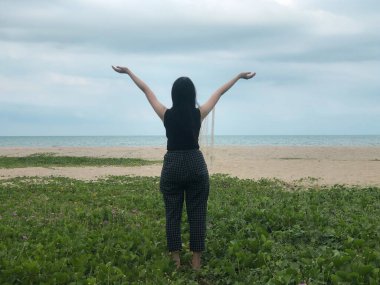 Yeşil çimlerin üzerinde duran bayanın arkası, ellerini havaya kaldır, tatilde dinlenme zamanı.