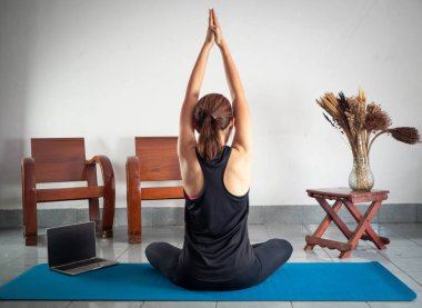 Egzersiz kıyafeti giyen bir kadının arka tarafı, evdeki yoga minderinde vücut geliştirmek için ellerini kaldır, dinlenme zamanı.