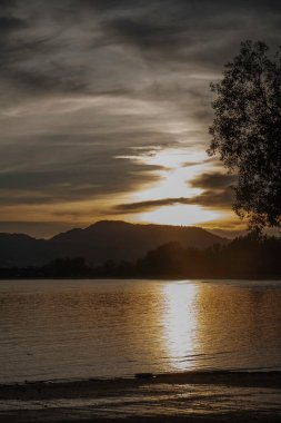 Güzel göl manzarası, gün batımından önce, güneş ışığının yansıması su yüzeyinde parlayan dağın üzerinde, huzurlu ve romantik bir duygu.
