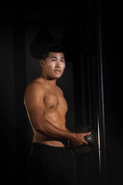 Yakışıklı adam topu elinde tutuyor, kasları için egzersiz yapıyor, formda ve sıkı vücut, modellik yapıyor.