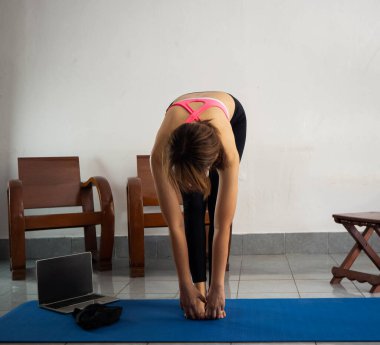 Egzersiz kıyafeti giyen kadın ayakta duruyor ve vücudunu eğiyor, yoga minderinde vücut çalışıyor, dinlenme zamanı.