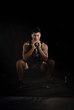 Elinde dambıl tutan yakışıklı adam, kaslı, formda ve sıkı vücut için egzersiz yapıyor.