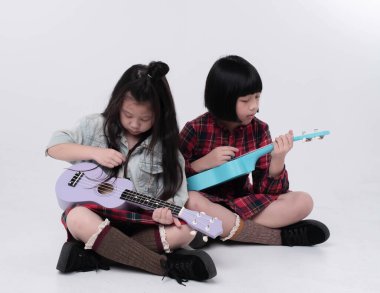 Zemin katta oturan iki kız kardeş, ilginç duygularla ukulele çalıyorlar, birlikte hareket ediyorlar.