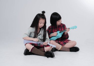 Zemin katta oturan iki kız kardeş, ilginç duygularla ukulele çalıyorlar, birlikte hareket ediyorlar.