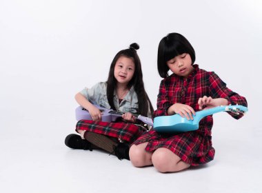 Zemin katta oturan iki kız kardeş, ukulele 'yi ellerinin arasında tutuyorlar, ilginç duygularla, birlikte hareket ediyorlar.