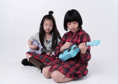 Zemin katta oturan iki kız kardeş, ilginç duygularla ukulele çalıyorlar, birlikte hareket ediyorlar.