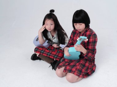 Zemin katta oturan iki kız kardeş, ukulele 'yi ellerinin arasında tutuyorlar, ilginç duygularla, birlikte hareket ediyorlar.