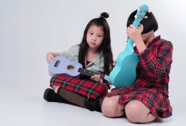 Zemin katta oturan iki kız kardeş, ukulele 'yi ellerinin arasında tutuyorlar, ilginç duygularla, birlikte hareket ediyorlar.