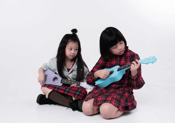 Two sisters sitting on ground floor,play ukulele with interested feeling,doing activity together