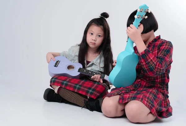 Zemin katta oturan iki kız kardeş, ukulele 'yi ellerinin arasında tutuyorlar, ilginç duygularla, birlikte hareket ediyorlar.