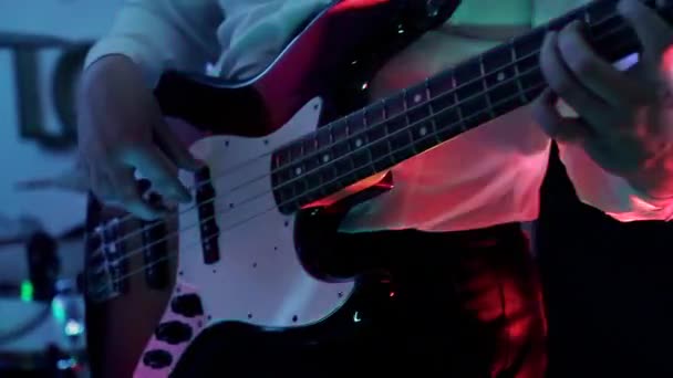 Музичне відео панк, хеві-метал або рок-гурт. Крупним планом чоловічі руки грають на бас-гітарі в прямому ефірі під час шоу в блакитному неоновому світлі. Концерт у нічному клубі. Музикант грає на бас-гітарі — стокове відео