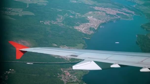 Flügel eines Flugzeugs Blick aus dem Fenster des Flugzeugs fliegen über die Stadt und den Fluss. Flugzeugflug. Flugreisen. Blick auf die Erde vom Himmel — Stockvideo