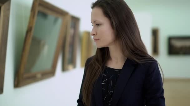 Mulher bonita elegante olha para as imagens no Museu de Arte Moderna. Close-up Jovem Assistindo Fotos na Galeria de Fotos. Obra de Pinturas de Arte na Exposição na Galeria de Arte da Cidade . — Vídeo de Stock