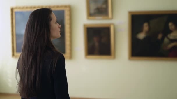 Женщина смотрит на картины в Музее современного искусства. Молодая девушка смотрит работы художников на выставке в Городской картинной галерее. — стоковое видео