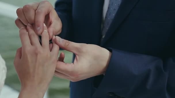 The groom wears a wedding ring on the brides finger. Wedding ceremony near the water. Marriage hands with rings close up. Bride and groom exchange wedding rings. — Stock Video