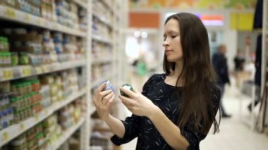 Genç anne çocuk için bebek maması, püre ve meyve suyu seçer ve almayı düşünür. Bir bebeğe bakma kavramı. Kadın süpermarket rafının yanında duruyor ve ürünleri seçiyor..