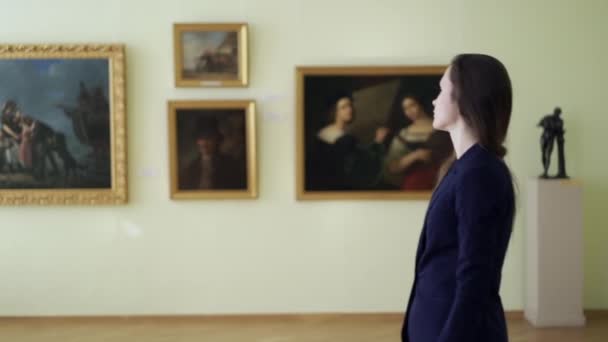 Elegant Girl regarde les images dans le Musée d'Art Moderne. Paintings in Gallery During Art Exposition. Une jeune femme regarde des œuvres d'art Peintures sur l'exposition au Musée des beaux-arts de la ville. — Video