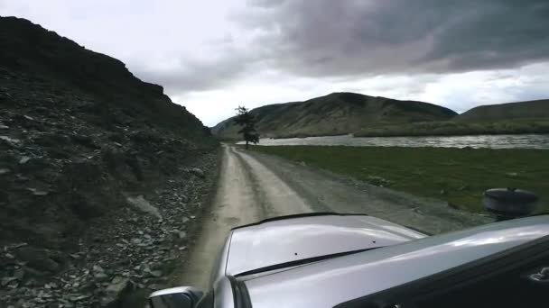 SUV rijdt over een hoge bergweg over een bergrivier. Auto reizen: een grote auto gaat vooruit platteland. Buiten de weg reizen op de berg. Auto passeren in hoge berg weg in de zomer. Stockvideo's