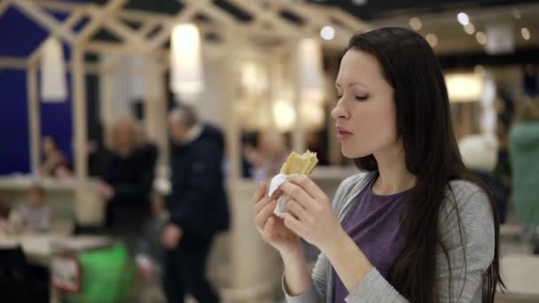 Fast food restoranında lezzetli olmayan sosisli yiyen genç bir kadın. Ucuz abur cubur yemek, yüksek kalorili abur cubur bağımlılığı. Yakın plan aç bir kadın alışveriş merkezinde yemekhaneyi çiğniyor. — Stok video