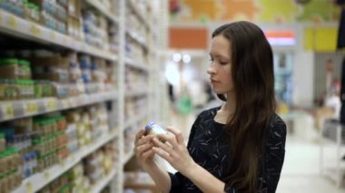 Anne, bebek maması, püre ve meyve sularını pazar yerinden seçer ve almayı düşünür. Kadın süpermarket rafının yanında duruyor ve ürünleri seçiyor.