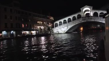 Büyük Kanal, Venedik 'te gece aydınlatması. İtalya 'daki Rialto Köprüsü' nün gece manzarası çok güzel. Sudaki yansımalar. Köprüde turistler var. İnanılmaz manzara..