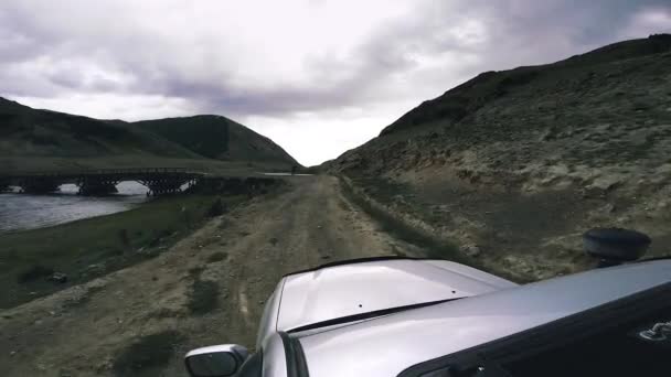 Auto reizen: een grote auto gaat vooruit platteland. SUV rijdt over een hoge bergweg over een gevaarlijke bergrivier in een canyon. POV - Standpunt van een auto die in de bergen over de weg rijdt. — Stockvideo