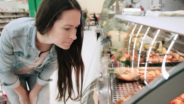 Vrouw selecteert gebraden kip in de supermarkt. Mooie dame in casual kleding kiest geroosterd vlees op de markt en denken te kopen. Fast food kip grill — Stockvideo