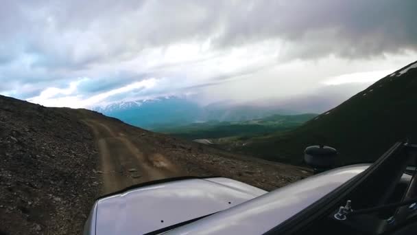 Conduzca un coche cuesta arriba en un día nublado. Auto viaje: POV - Punto de vista SUV recorre un valle con montañas en el campo. Viaje fuera de carretera. Concepto de viaje en coche. — Vídeo de stock