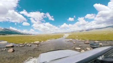 SUV derin bir nehir akışında ilerliyor. Dağ yolunda araba gezintisi. Otomatik seyahat: POV - Varış noktası kırsal alanda hareket ediyor. Yol dışı seyahat. Araba yolculuğu konsepti.