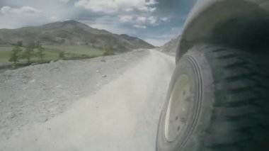  Vadi boyunca seyahat eden bir arabanın tekerleğinin görüntüsü. Araba engebeli bir kır yolunda hızlı gider. Kırsal kesimde yüksek bir dağ yolunda arazi aracı sürüyor. Otomatik seyahat: dağda yolculuk dışı. 