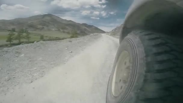 Utsikt över hjulet på en bil som färdas längs en dal. Bilen färdas snabbt på en tuff landsväg. SUV rider på en hög bergsväg på landet. Auto resa: off the road resa på berget. — Stockvideo