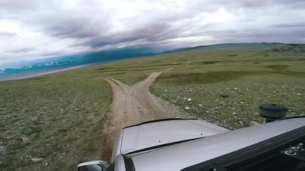 Voyage en voiture : SUV parcourt une vallée avec une rivière et des montagnes à l'horizon. POV - Point de vue voiture se déplaçant le long de la route vers les montagnes à travers la campagne. Voyage hors route. Concept de voyage voiture . — Video