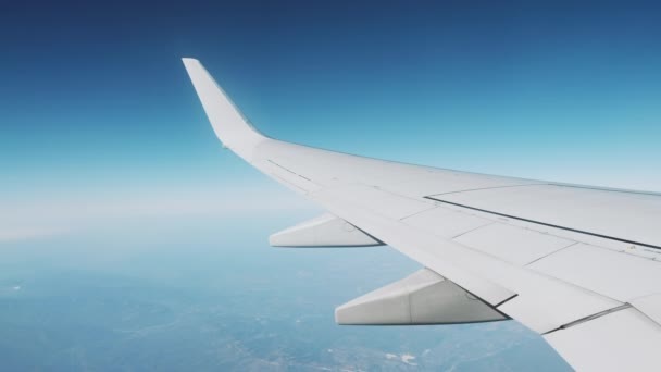 Cestování letadlem za jasného slunečného dne. Pohled z okna létajícího letadla na modré obloze a vysokých horách. Scénický pohled z létajícího letadla — Stock video