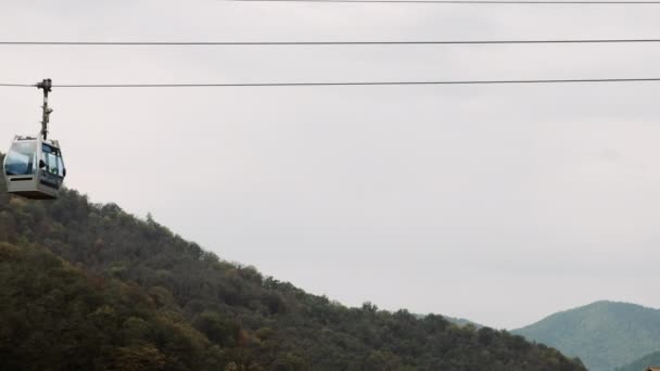 Ascensor de esquí vía cable para el transporte de personas en la montaña de verano. Telesilla en la colina, cielo gris. Teleférico levanta turistas en resort de lujo — Vídeo de stock