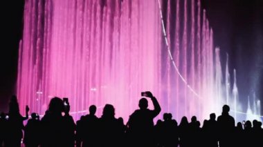 Işık festivali sırasında renkli çeşmeler. Bir grup insan şehir gece manzarasının, ışığın ve fıskiyenin tadını çıkarıyor. İnsan siluetleri.