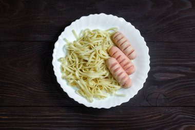 koyu ahşap arka planda beyaz plaka sosis ve spagetti