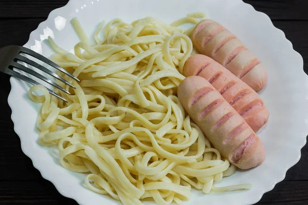 Sausages and spaghetti in white plate on dark wooden background — Stock Photo, Image