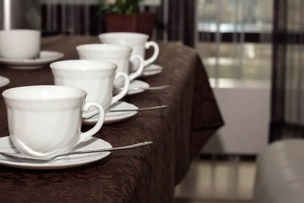 white cups of tea are in a row on the table with a brown tablecloth