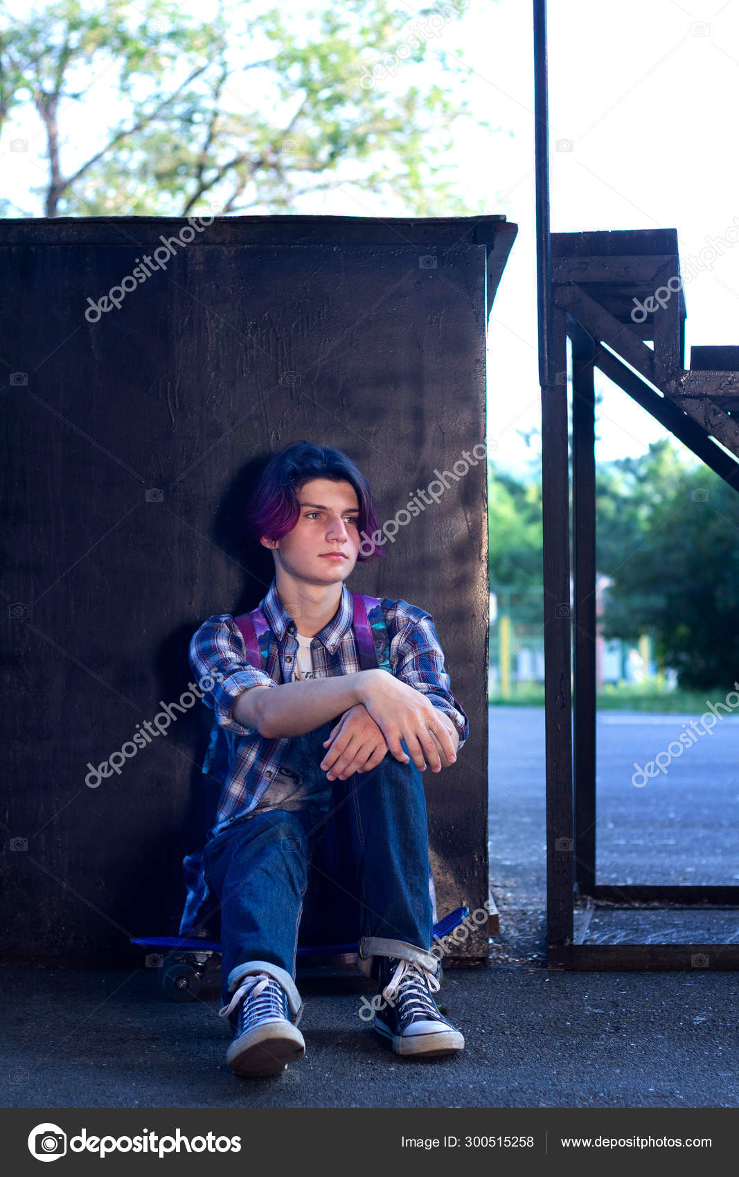 A Young Guy With Purple Hair Sits On A Skateboard In The Park On