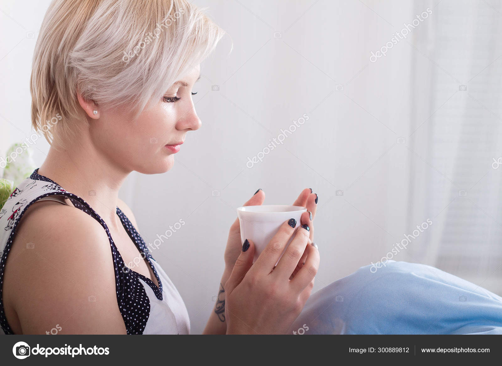 Young Beautiful Blonde Girl With Short Hair Sitting On Her Bed And