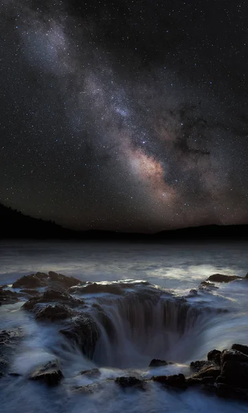 Thor\'s well under milky way with mountains in the background. Long exposure with silky water floating into the hole.