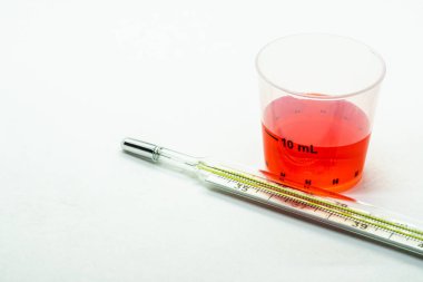 Termometre Kupası beyaz arka plan üzerinde izole kırmızı ilaç şurubu ile yanındaki.
